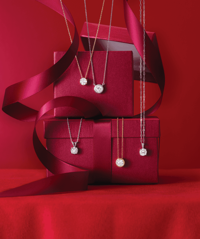 Motek Jewelry diamond solitaire halo pendant necklaces in white and yellow gold on crimson gift boxes.