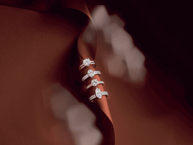 Four stacked Motek Jewelry diamond engagement rings in white and yellow gold displayed on an elegant copper-brown satin ribbon.