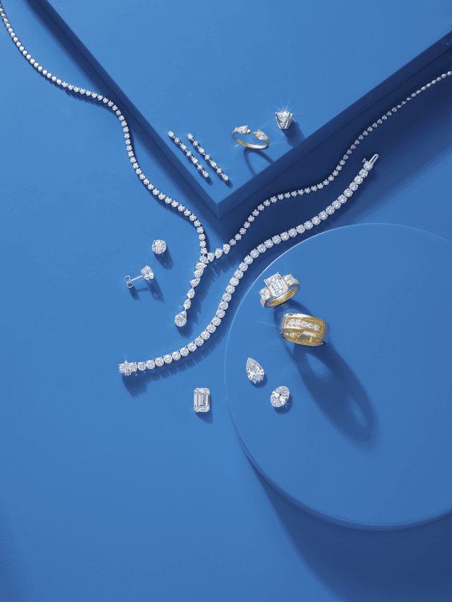 Motek Jewelry diamond tennis necklaces, rings, stud earrings, and loose stones styled on vibrant blue circular pedestals.