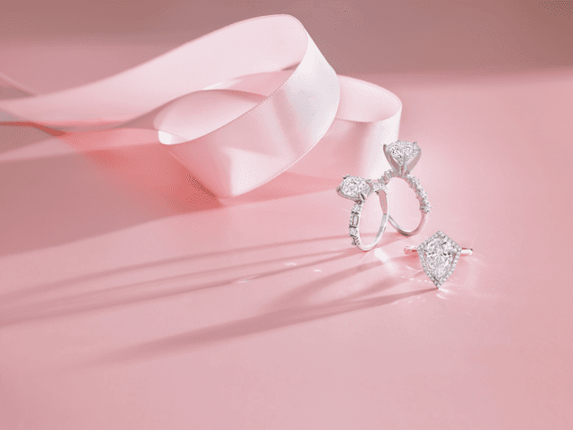 Motek Jewelry pear and round-cut diamond engagement rings casting soft morning shadows beside a light pink satin ribbon.