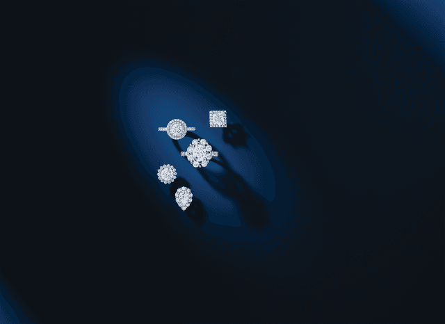 Motek Jewelry loose and set diamonds showcasing halo, round, emerald, and pear cuts under blue spotlight.