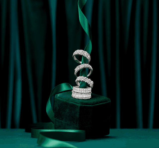 Stack of four Motek Jewelry diamond eternity rings spiraling up an emerald green ribbon and velvet display pedestal.