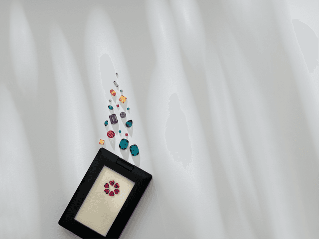 Colorful collection of loose sapphire, ruby, and emerald gemstones bursting out of a sleek Motek Jewelry presentation case.