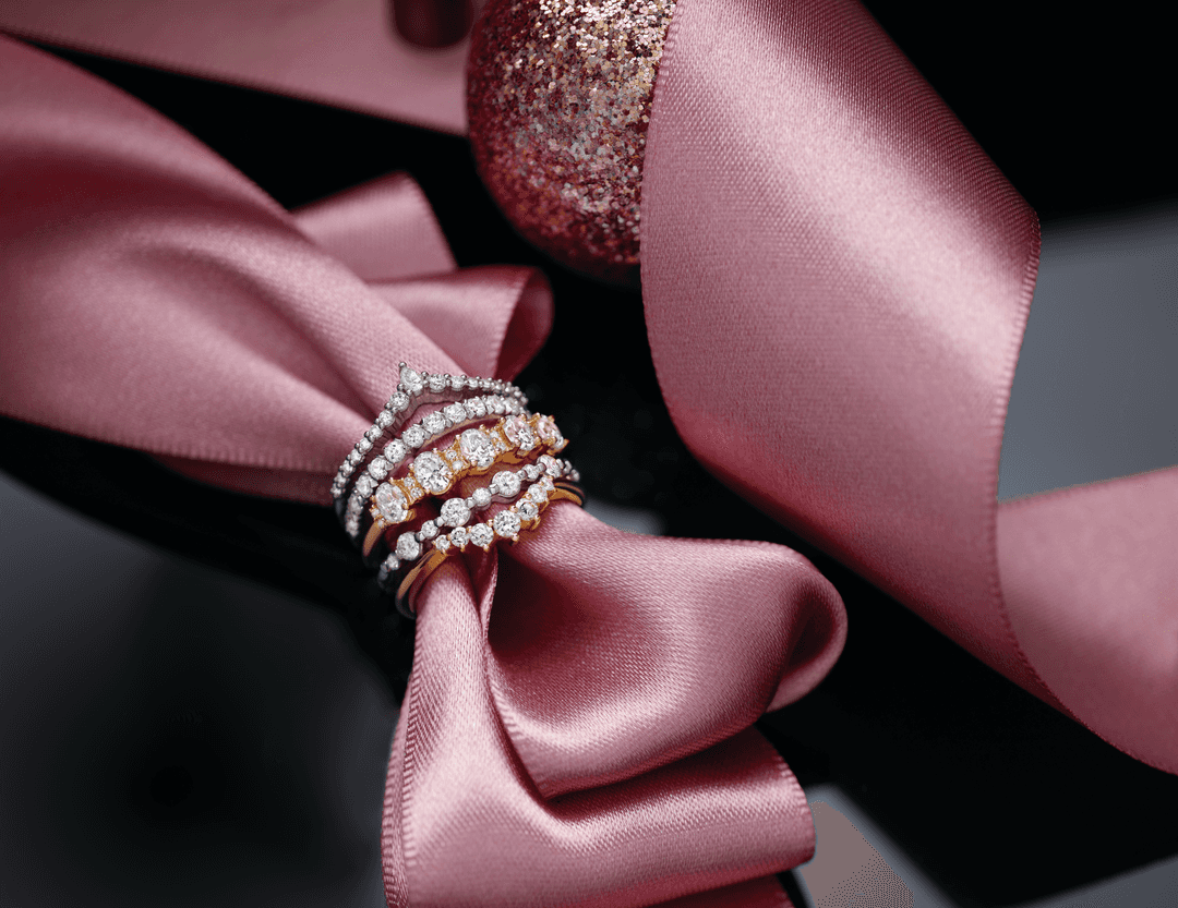 Stack of Motek Jewelry diamond and yellow gold wedding bands wrapped around a shimmering pink silk ribbon, featured on himish.com.