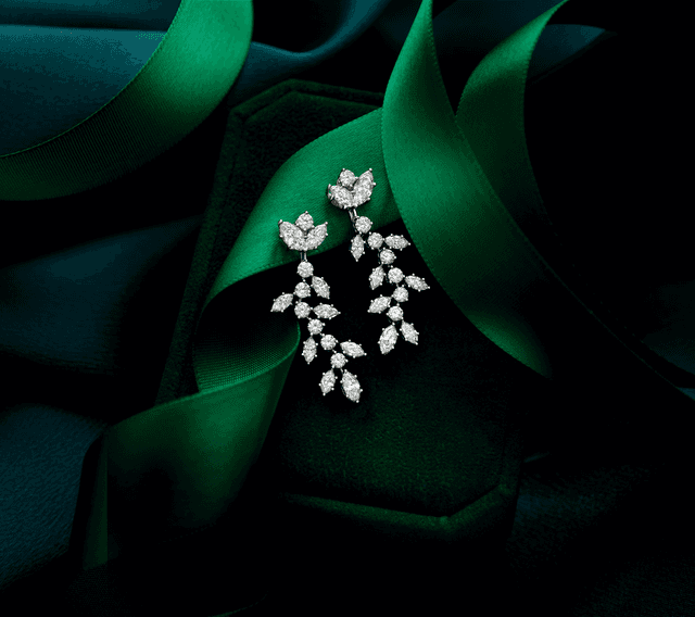 Elegant Motek Jewelry marquise and round diamond chandelier drop earrings resting on luxurious emerald-green draped satin fabric.