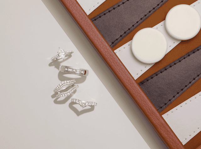 Motek Jewelry marquise and round diamond wedding bands and curved contour rings beside a leather case.